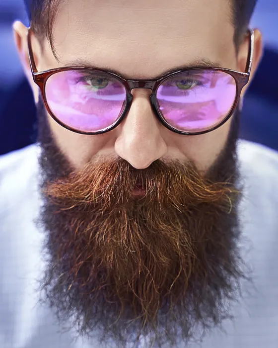 Gerahmter Druck : Bartiger Mann mit Brille mit Bildschirmreflex arbeitet an Computer in IT-Büro. Gerahmter Druck : Bartiger Mann mit Brille mit Bildschirmreflex arbeitet an Computer in IT-Büro.