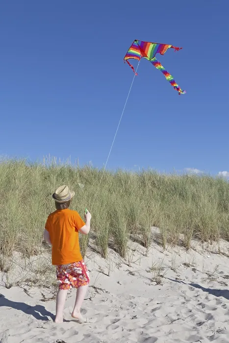 Gerahmter Druck : Ein Junge spielt mit einem Drachen am Strand.
