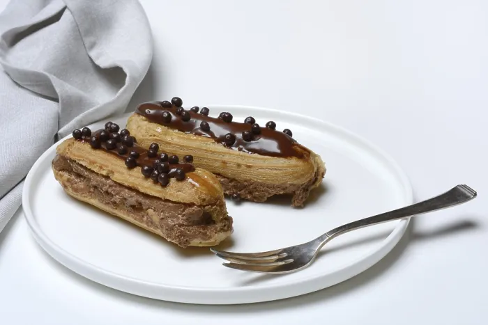 Gerahmter Druck : Zwei Schokoladen-Eclairs auf einem Teller. Gerahmter Druck : Zwei Schokoladen-Eclairs auf einem Teller.