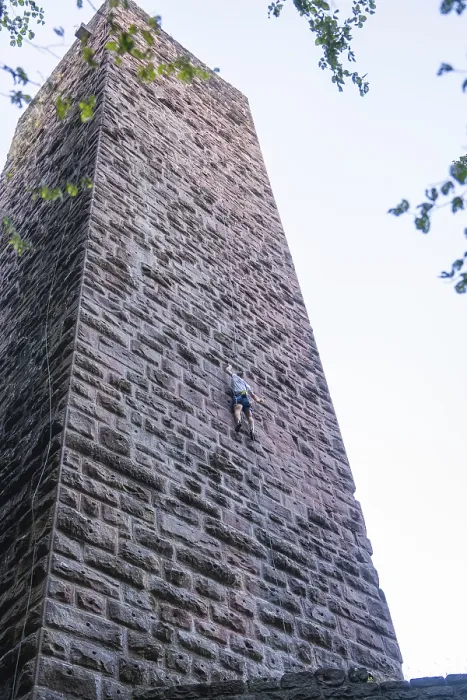 Gerahmter Druck : Ein Kletterer klettert an der Steinmauer eines Turms. Gerahmter Druck : Ein Kletterer klettert an der Steinmauer eines Turms.