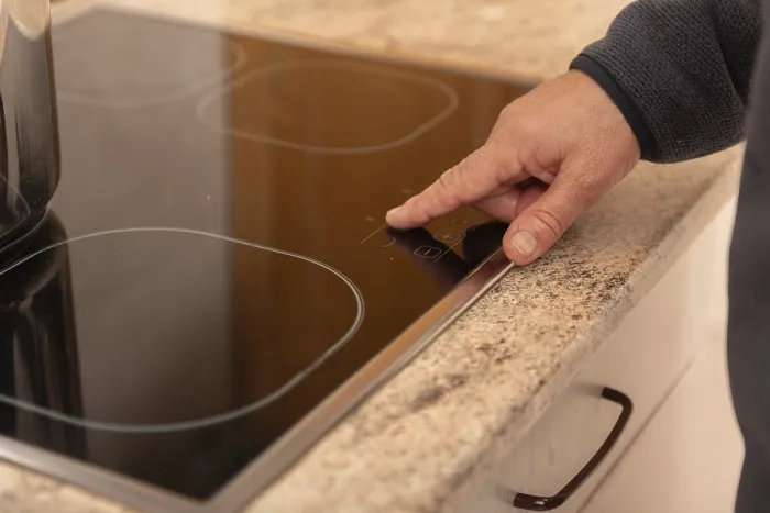 Gerahmter Druck : Ein Nahblick auf eine Hand, die das Touchscreen-Steuerungselement eines modernen Induktionsherdtops verwendet. Gerahmter Druck : Ein Nahblick auf eine Hand, die das Touchscreen-Steuerungselement eines modernen Induktionsherdtops verwendet.