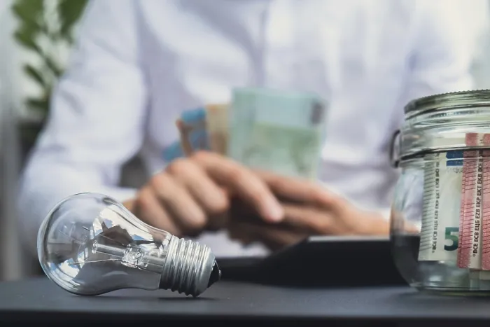 Gerahmter Druck : Elektrische Glühbirne. Ein Mann zählt Ausgaben auf Rechnungen von Strombanknoten in Euro Bargeld auf einem Kalkulator. Gerahmter Druck : Elektrische Glühbirne. Ein Mann zählt Ausgaben auf Rechnungen von Strombanknoten in Euro Bargeld auf einem Kalkulator.