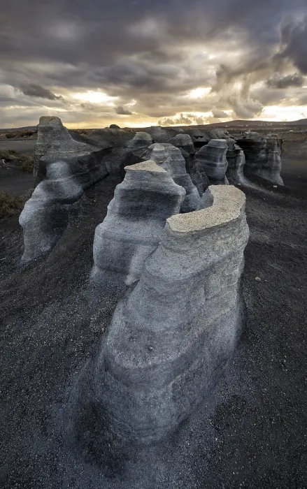 Gerahmter Druck : Erosionsschuttformationen, vulkanische Landschaft mit dramatischem wolkenverhangenen Himmel am Sonnenuntergang. Gerahmter Druck : Erosionsschuttformationen, vulkanische Landschaft mit dramatischem wolkenverhangenen Himmel am Sonnenuntergang.