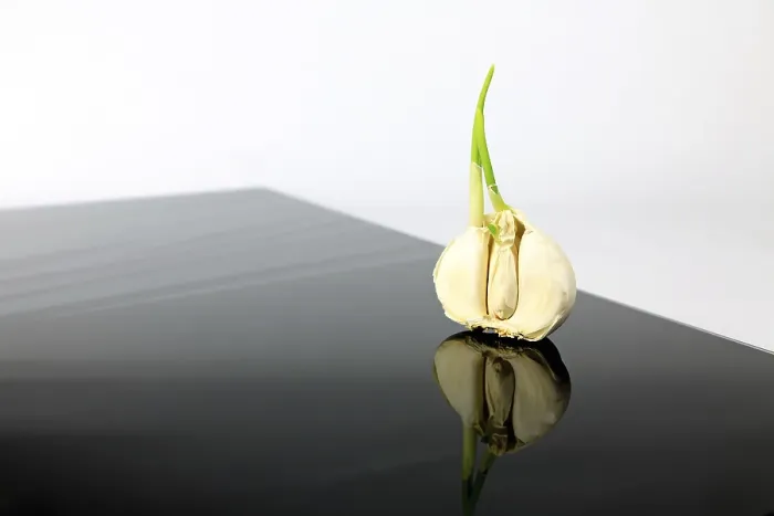 Gerahmter Druck : Knoblauch auf einem schwarzen Teller mit reflektierendem Effekt.