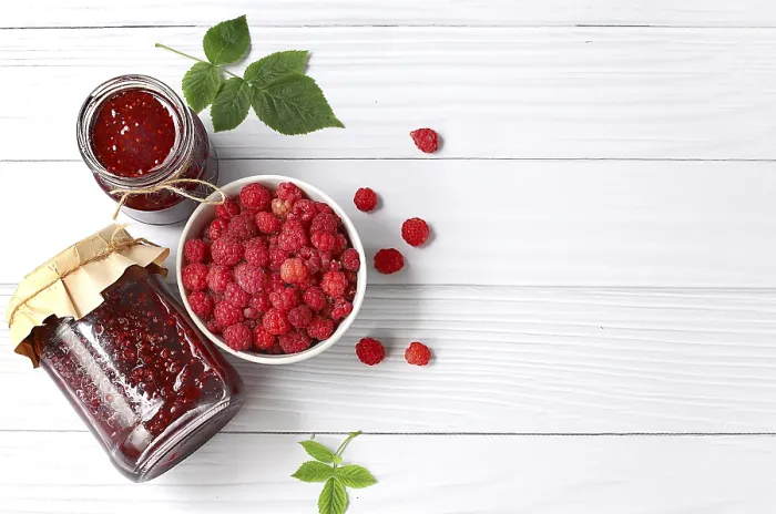 Gerahmter Druck : Dosen mit Himbeermarmelade auf einem hellen Holzboden mit Blättern. Gerahmter Druck : Dosen mit Himbeermarmelade auf einem hellen Holzboden mit Blättern.