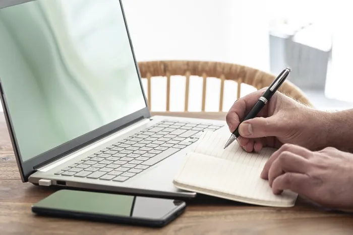 Gerahmter Druck : Ein Mann nimmt Notizen auf Papier, während er einen Laptop verwendet. Gerahmter Druck : Ein Mann nimmt Notizen auf Papier, während er einen Laptop verwendet.