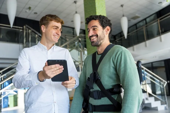 Gerahmter Druck : Mechanischer Exoskelett, Physiotherapeut sieht sich bei Beratung mit Tablet mit behindertem Menschen mit Roboter-Skelett. Gerahmter Druck : Mechanischer Exoskelett, Physiotherapeut sieht sich bei Beratung mit Tablet mit behindertem Menschen mit Roboter-Skelett.
