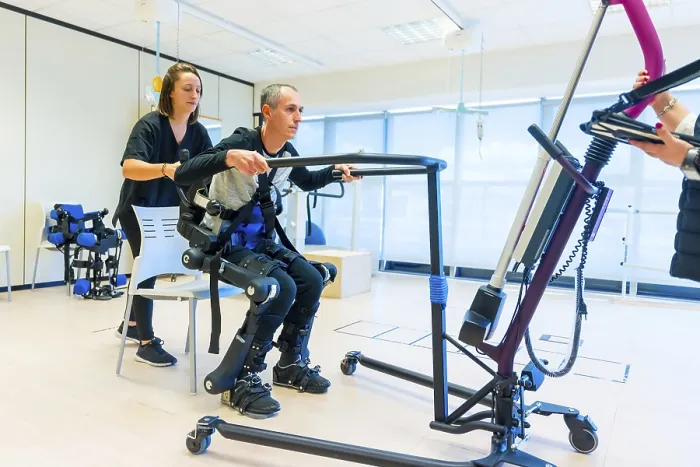 Gerahmter Druck : Mechanischer Exoskelett. Weibliche Physiotherapie-Heilerziehungspflegerin hebt behindertes Kind mit roboterischem Skelett auf. Gerahmter Druck : Mechanischer Exoskelett. Weibliche Physiotherapie-Heilerziehungspflegerin hebt behindertes Kind mit roboterischem Skelett auf.