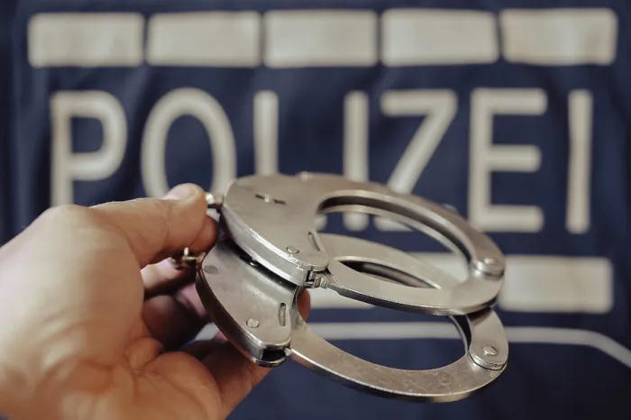 Gerahmter Druck : Ein Paar Handschellen wird von einer Hand gehalten. Gerahmter Druck : Ein Paar Handschellen wird von einer Hand gehalten.