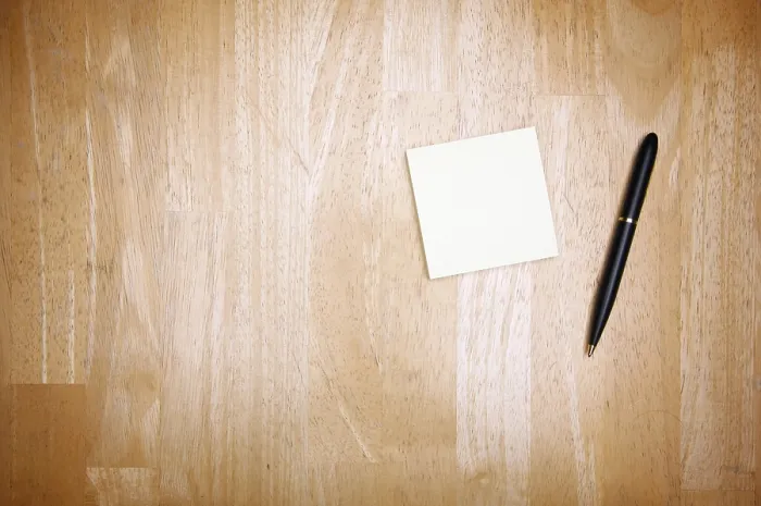 Gerahmter Druck : Feder und Post-it-Notizblock gegen einen Holz-Hintergrund.