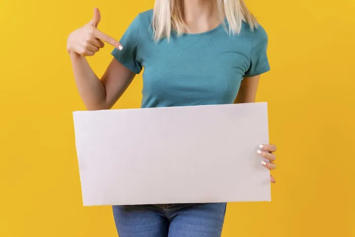 Gerahmter Druck : Blonde Mädchen auf gelbem Hintergrund, das auf eine leere Werbeplakat zeigt. Gerahmter Druck : Blonde Mädchen auf gelbem Hintergrund, das auf eine leere Werbeplakat zeigt.