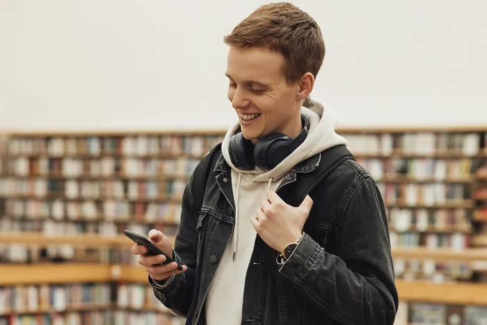 Gerahmter Druck : Lächelnder Student verwendet Smartphone, während er in der Bibliothek steht. Gerahmter Druck : Lächelnder Student verwendet Smartphone, während er in der Bibliothek steht.