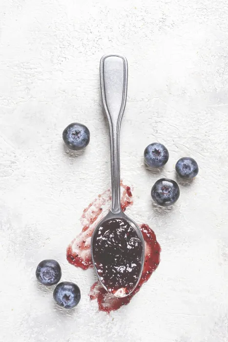 Gerahmter Druck : Ein Löffel mit Blaubeerenmarmelade, auf einem weißen Tisch. Gerahmter Druck : Ein Löffel mit Blaubeerenmarmelade, auf einem weißen Tisch.