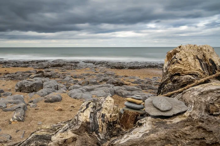 Gerahmter Druck : Ein Steinhaufen auf einem Baumstamm, unter einem dramatischen Himmel auf einer steinigen Strand. Gerahmter Druck : Ein Steinhaufen auf einem Baumstamm, unter einem dramatischen Himmel auf einer steinigen Strand.
