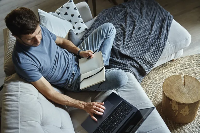 Gerahmter Druck : Oberer Blick auf einen Mann, der auf einem Sofa sitzt und ein Laptop benutzt.
