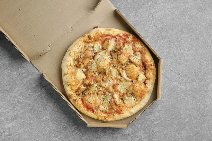 Gerahmter Druck : Ein Pizza mit Hähnchen, Käse und Ananas in einer Kartonbox.