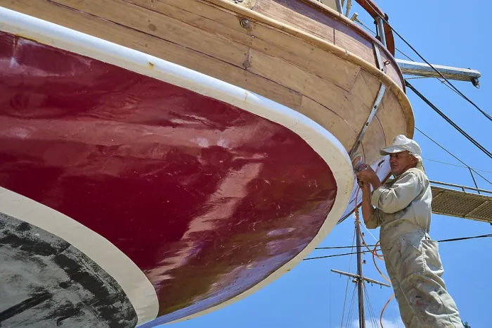 Gerahmter Druck : Ein Arbeiter arbeitet an der roten Hülle eines Segelschiffs. Gerahmter Druck : Ein Arbeiter arbeitet an der roten Hülle eines Segelschiffs.