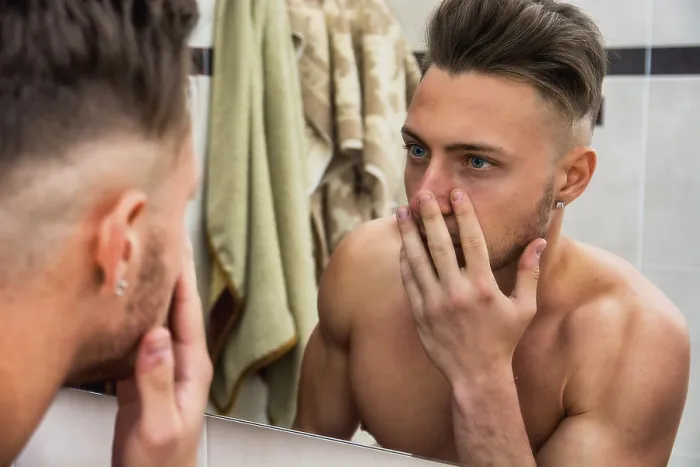 Gerahmter Druck : Jüngerer Mann berührt sein Gesicht, während er sich im Spiegel betrachtet. Gerahmter Druck : Jüngerer Mann berührt sein Gesicht, während er sich im Spiegel betrachtet.