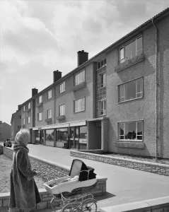 Drucke von CHEPSTOW, WALES. Eine Aussicht auf einen Block von Easiform-Wohnflächen mit einem Laden im Erdgeschoss in Chepstow, der eine Frau vorne mit dem Kinderwagen treibt England damals und heute – Historischer Wandel im Laufe der Zeit: Flachmöbel EASIFORM JLP 01/08/06 5725