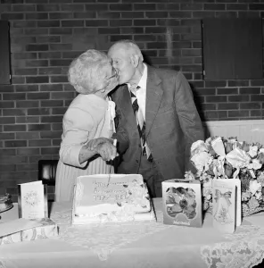 Drucke von Laing Sports Ground, Rowley Lane, Elstree, Barnet, Greater London. Herr und Frau Stanborough küssen sich beim Einschneiden eines Kuchens während einer Überraschungsparty zum goldenen Hochzeitstag England damals und heute – Historischer Wandel im Laufe der Zeit: Küsse JLP01_09_870580