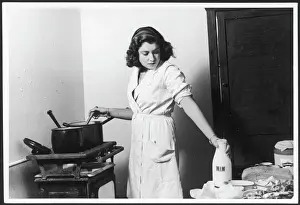 Drucke von Eine Haushausfrau kocht auf einem einfachen Ofen im spartanischen und strengen Küchendach mit Milch zum Gebraten Küche Drucke: Die 1940er Haushälterin Küche