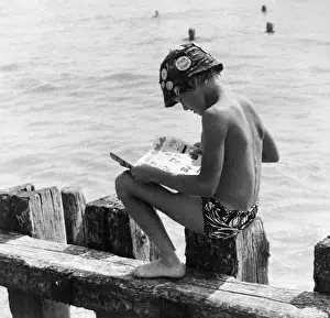 Childhood In The Sixties Drucke: Boy sitting on breakwater reading a comic