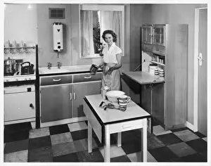 Drucke von Die Frau genießt das Kochen in ihrem neuen Küchenraum, der mit allen neuesten Modellen ausgestattet ist Küche Drucke: Spätestes 1950er Küchenstil