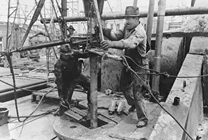 American Oil Industry Drucke: Oil field workers adding a length of pipe to drill stream by