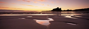 Northumberland Coastline Views Drucke: Bamburgh castle in silhouette at sunrise, with rock pools on empty beach