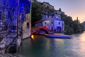 Boot in Bewegung unter der beleuchteten Nesso-Brücke, Lago di Como, Lombardei, italienische Seen.