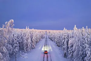 Überblicksansicht eines Autos mit leeren Reifen auf einer eisigen und schmalen Straße unter beleuchteten Scheinwerfern in Akaslompolo im Kolari im Pallas-Yllastunturi Nationalpark in der Lapplandregion Finnland Europa