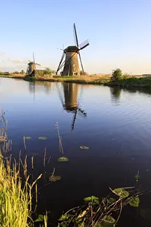 South Holland Travel Destination Drucke: Typical windmills reflected in the canal framed by grass in spring, Kinderdijk, UNESCO