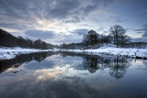 Blick des Winterwassers von River Brathay zum Morgen, unter Schnee mit Reflexionen in der Nähe von Elterwater-Village