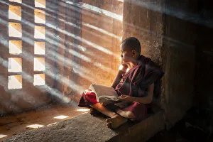 Ein junger Mönch liest vor einem Fenster in einer Tempelhalle der UNESCO im Shan State von Myanmar