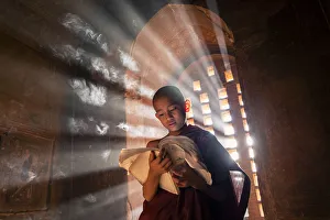 Ein junger Mönch liest vor einer Fensterseite in einem Tempel innerhalb der UNESCO-Bagans im Shan State von Myanmär