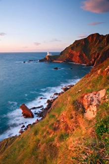 North Devon Beaches Drucke: View of sea cliffs with distant lighthouse at sunset