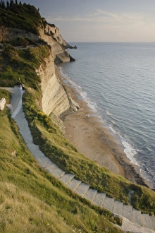 Corfu Beach Drucke: View of steps down to beach from steep cliffs in evening sunlight