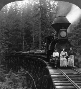 Brücke Drucke: OREGON: HOLZLOGGEFAHRTEN ZWEI FRAUEN UND EIN MANN SITzen vor einer Holzloggefahrt mit flachen Wagen beladen mit