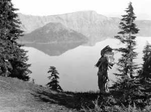 Edward S Curtis Photos Drucke: KLAMATH CHIEF, c1923. A Klamath chief in a ceremonial headdress standing on a hill overlooking Crater Lake in Oregon