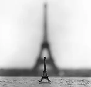 Drucke von Schwarzes und weißes Bild einer Figur der Eiffelturm-Skulptur sitzt auf einem Gurt im Trocadéro, mit Schatten des echten Eiffelturms hinter ihr Internationale Architektur Drucke: Die Eiffelturm, groß und klein