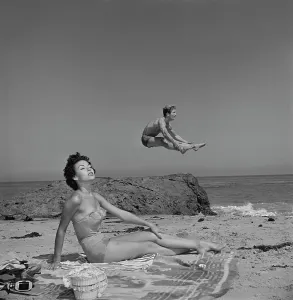 Drucke von Puerto-ricanische Schauspielerin Rita Moreno sonnt sich, während der amerikanische Schauspieler Steve Rowland im Hintergrund springt, auf einer Strand, USA, um 1950 Rita Drucke: Moreno und Rowland