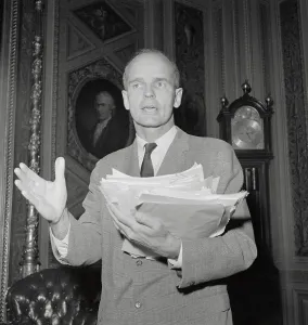 William Proxmire hält eine große Stapel von Dokumenten.