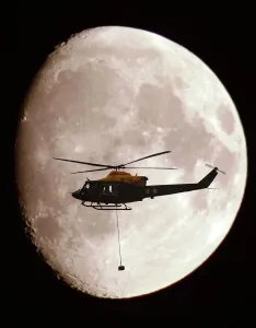Military Transport Helicopters Drucke: A Griffin Helicopter, with an underslung load, shown in silhouette against a full moon
