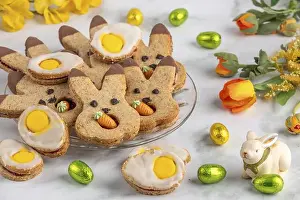 Eier- und Hasenbiskuits mit Süßcreme, neben Ostereiern und Frühlingsblumen