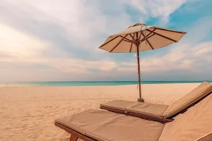 Schönes tropisches Sonnenuntergangslandschaft mit zwei Sonnensitzplätzen und Liegen unter einem Zelt. Weißer Sand am Meer mit Horizontansicht, farbenfroher Dämmerungsstimmung, Ruhe und Entspannung