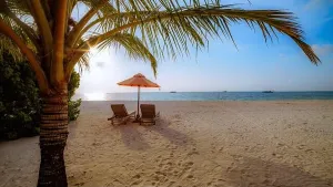 Schöne tropische Sonnenuntergangslandschaft mit zwei Sonnensitzen und Liegen unter Palmenbaum. Weißer Sand am Meer mit Horizontansicht zur See über dem bunten Dämmerungsgefühl der Zeit