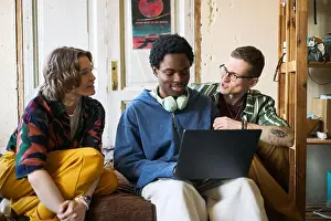 Vielfältige junge Erwachsene kooperieren auf Laptop, während sie zusammen sitzen.