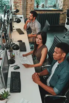 Blick von oben auf eine multikulturelle Mannschaft, die an Computern arbeitet und miteinander spricht, während sie in einem modernen offenen Raum sitzt.