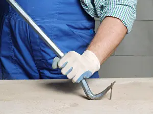 Arbeiter zieht einen Nagel aus einer Platte mit einem Brecheisen.