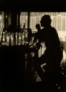 Ein Mann in Halbschatten sitzt vor dem Tresen eines Bars.
